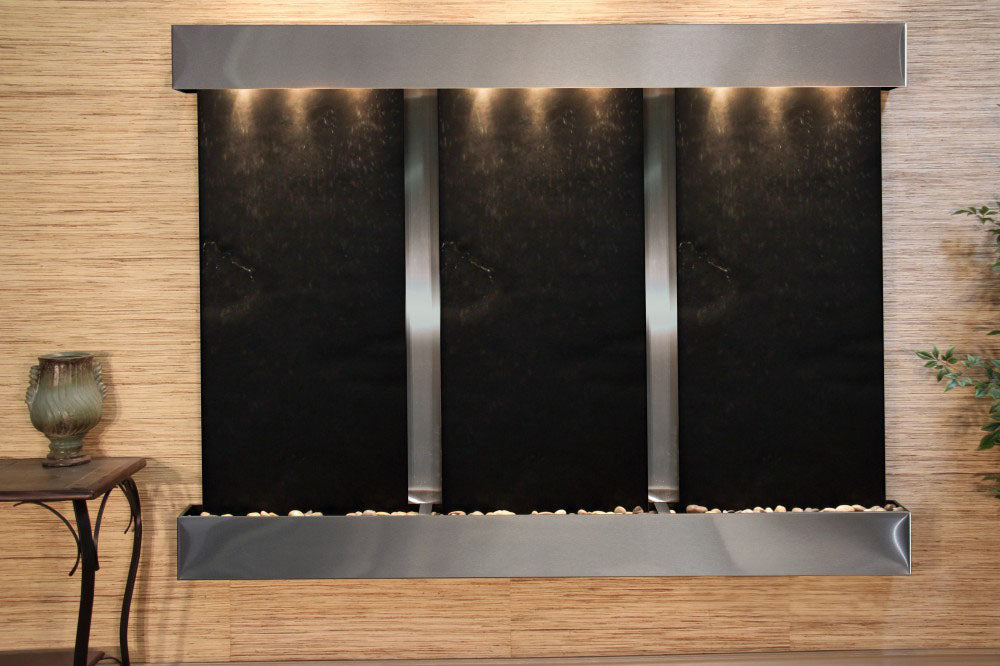 Modern indoor water feature with black panels and metallic base on a wooden wall.